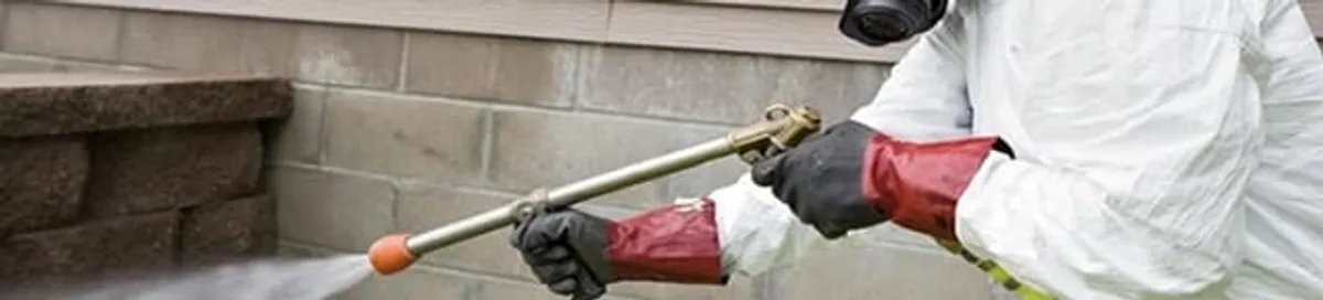 Pest control technician applying exterior insect treatment along a home foundation in Providence, RI