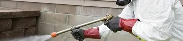Pest control technician applying exterior insect treatment along a home foundation in Providence, RI