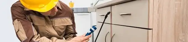 Roach exterminator applying treatment under kitchen cabinets in Providence, RI