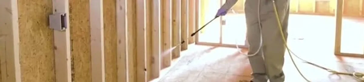 Termite treatment technician applying spray along framing and unfinished walls in Providence, RI