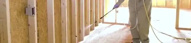 Termite treatment technician applying spray along framing and unfinished walls in Providence, RI